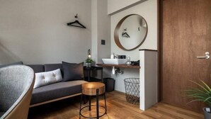 Un soggiorno moderno con un divano grigio, uno specchio rotondo, un tavolino in legno e un pavimento in legno.