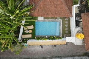 An aerial view of a rooftop pool area with a rectangular pool, lounge chairs, and a yellow sunshade.