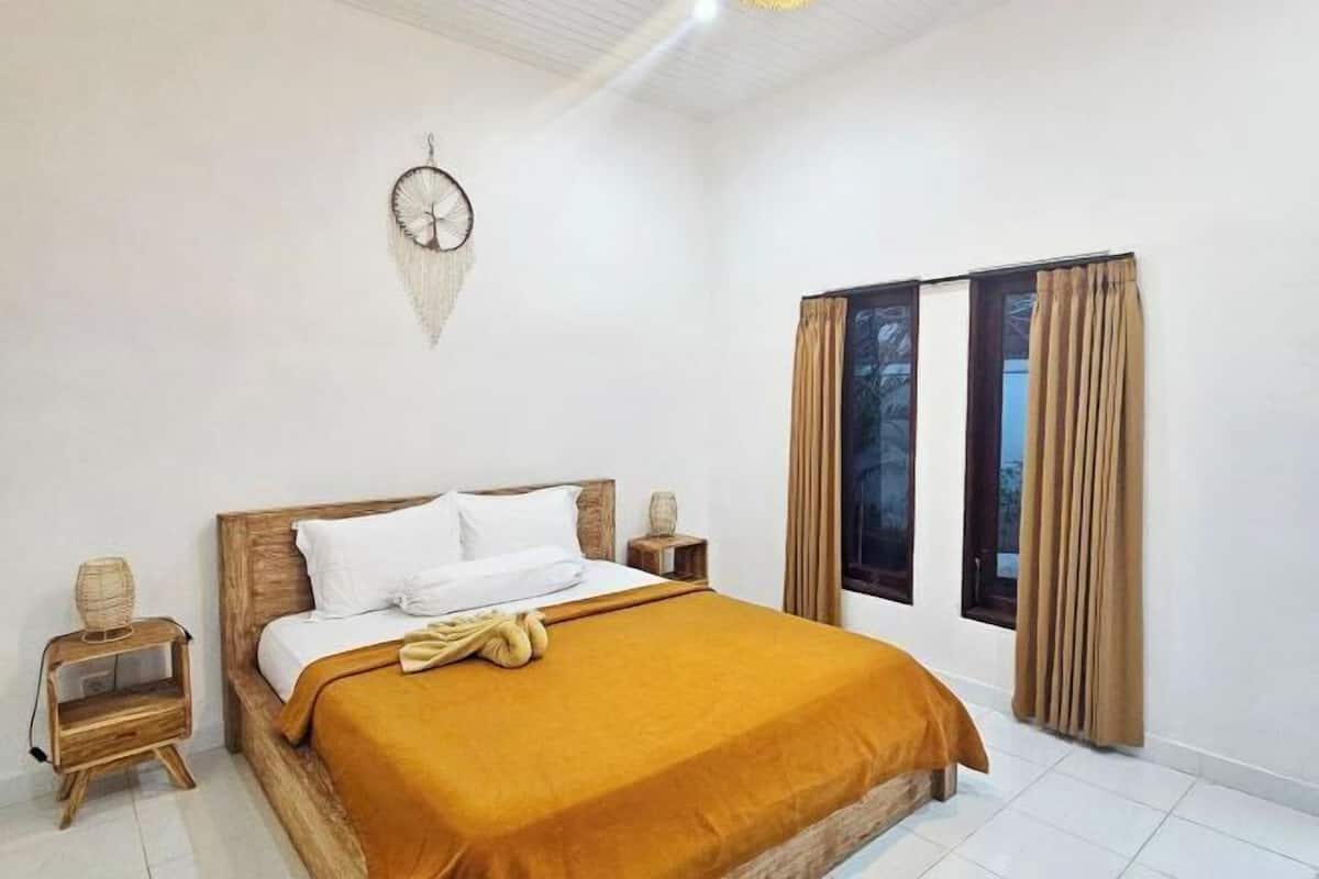 A bedroom with a wooden bed, white bedding, a brown throw, and a window with curtains.