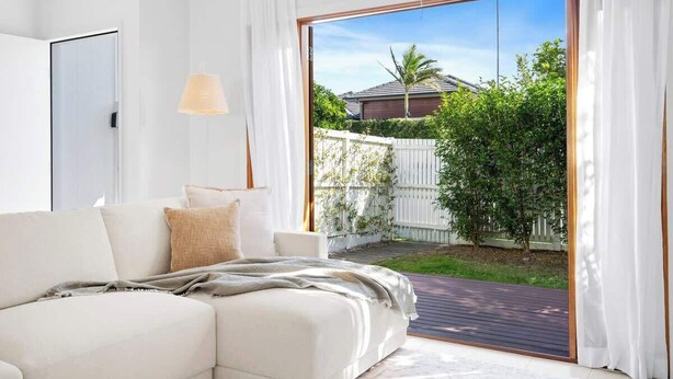 A bedroom with a bed, a sofa, and a large sliding glass door leading to a backyard. - Seabreeze (kingscliff)