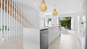A modern kitchen with a central island, white cabinetry, and a built-in dishwasher. - Seabreeze (kingscliff)