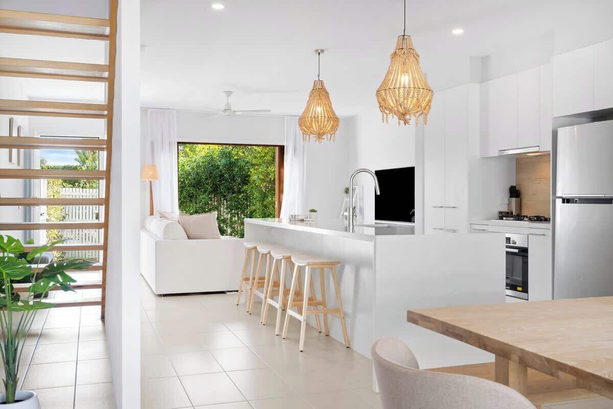 Una cocina moderna con armarios blancos, un refrigerador de acero inoxidable y una barra con taburetes.