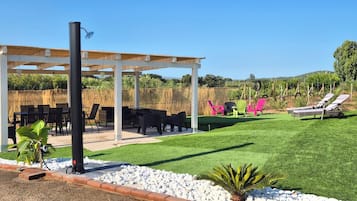 Uma área de estar coberta ao ar livre com mesas e cadeiras, um gramado e uma estrutura de pérgola.