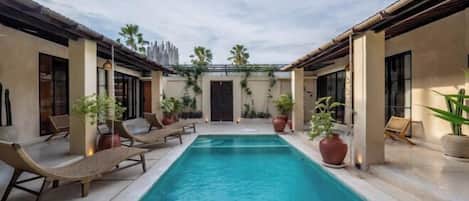 A swimming pool with lounge chairs and potted plants, surrounded by buildings with large windows and a pergola.
