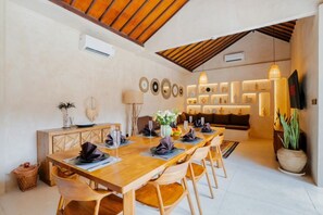 Un comedor con mesa de madera dispuesta para seis personas, rodeada de sillas, y una cocina moderna al fondo.