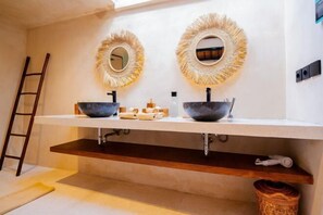 Un baño con dos espejos redondos, un estante de madera y una cesta tejida.