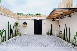 A courtyard with a black door, cactus plants, and a wooden fence. - Villa Terracotta by Pertama Stay (Bali)
