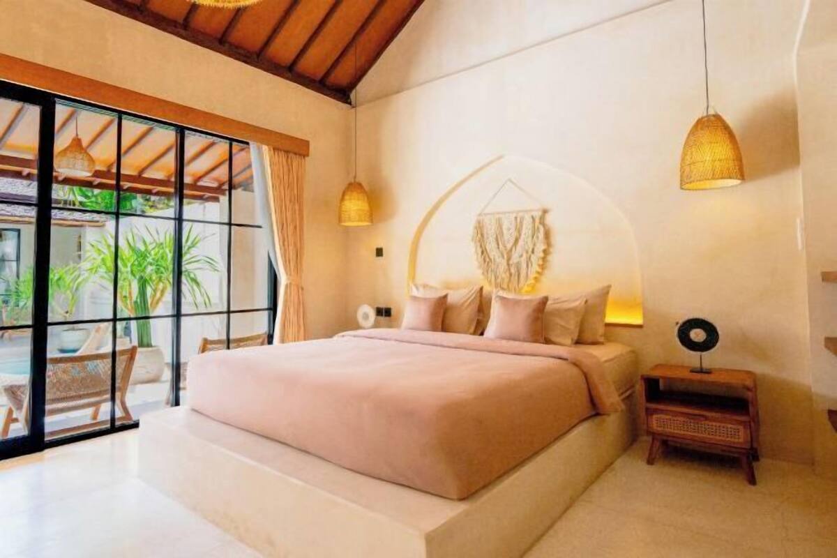 A spacious bedroom with a large bed, a small bedside table, and a hanging light fixture.
