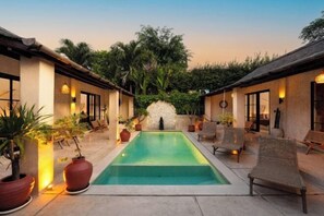 A pool area with lounge chairs, a stone wall, and potted plants. - Villa Terracotta by Pertama Stay (Bali)