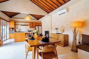 A spacious dining area with a long wooden table, chairs, and a hanging light fixture. - Villa Terracotta by Pertama Stay (Bali)