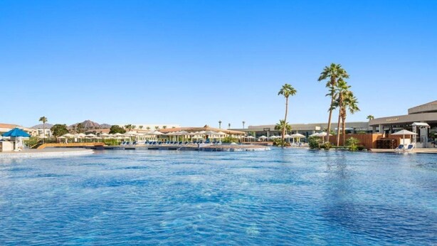 Ein großer Außenpool mit Liegestühlen und Palmen, umgeben von Hotelgebäuden.