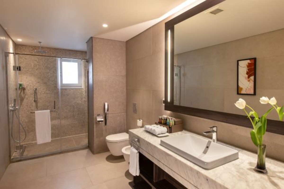 A modern bathroom with a glass-enclosed shower, a large mirror, and a marble sink.