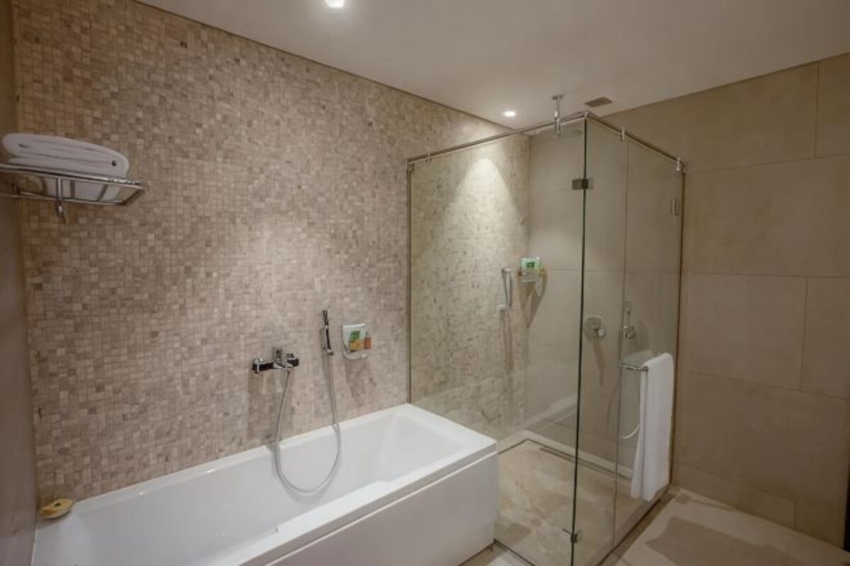 A modern bathroom with a glass-enclosed shower, a white bathtub, and a tiled wall.