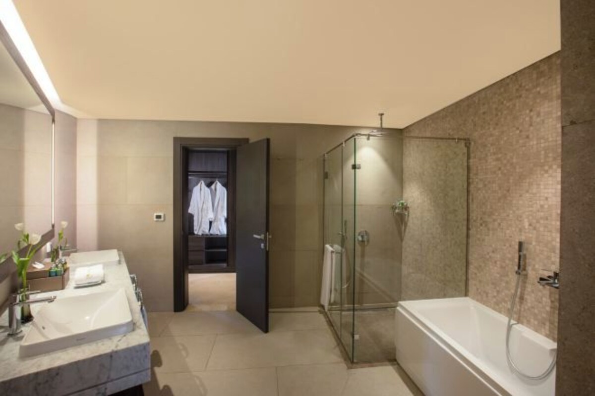A modern bathroom with a glass-enclosed shower, a large bathtub, and a vanity with two sinks.