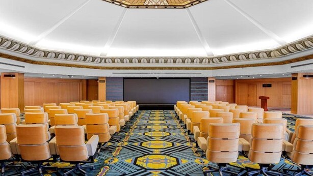 Un salón de conferencias con filas de sillas, una alfombra estampada y un techo decorativo.
