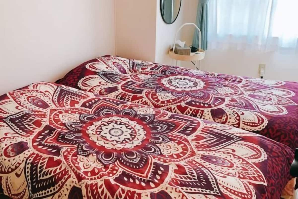 A room with a bed covered in a patterned bedspread, a bedside table with a lamp, and a mirror on the wall.
