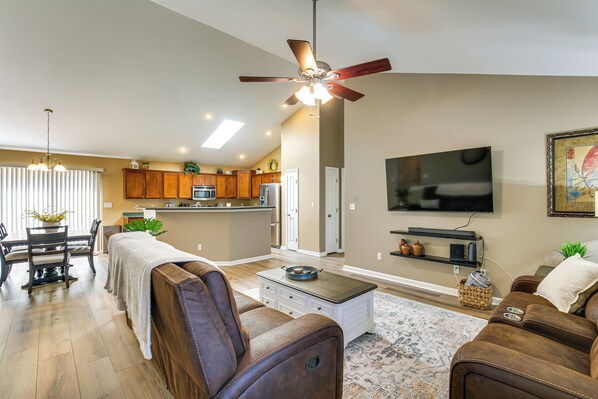 A spacious living room with a brown leather sofa, a coffee table, and a TV mounted on the wall. There is a ceiling fan, a dining area with a table and chairs, and a kitchen in the background. - Bar, Pool Table & Yard! Spacious Union Home (Union)