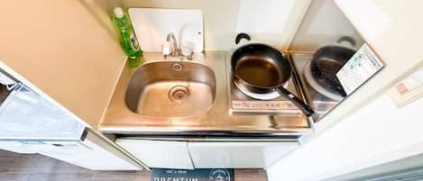 A compact kitchenette with a stainless steel sink, a pan, and a coffee maker.