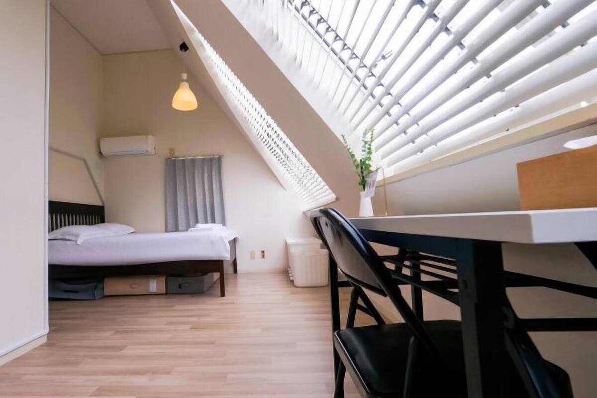 Ein modernes Zimmer mit Bett, Schreibtisch und einem Fenster mit Jalousien.
