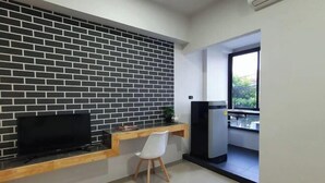 A modern room with a brick wall, a flat-screen TV, a wooden desk, and a white chair. - Irich residence (South Samrong) 6 Kms BTS-Pu Chao (Phra Pradaeng)