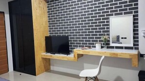 A room with a black and white brick wall, a wooden desk with a TV, a white chair, and a mirror. - Irich residence (South Samrong) 6 Kms BTS-Pu Chao (Phra Pradaeng)