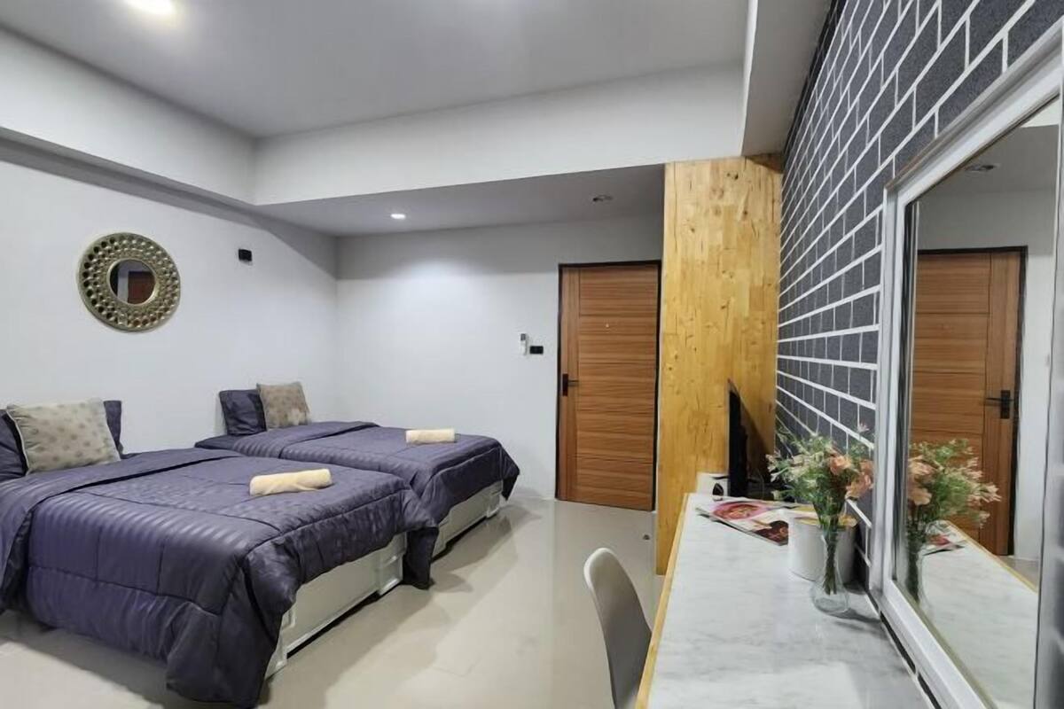 Un dormitorio moderno con dos camas, una pared de acento de madera, un espejo y una mesita con flores.