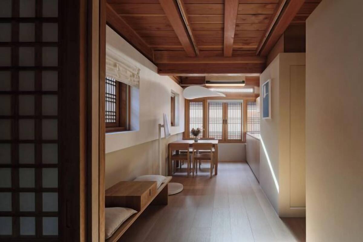 A narrow hallway with wooden flooring, a dining area with a table and chairs, and a traditional sliding door on the left.