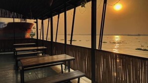 Un área de estar al aire libre con bancos de madera y vistas a la puesta de sol sobre el agua.