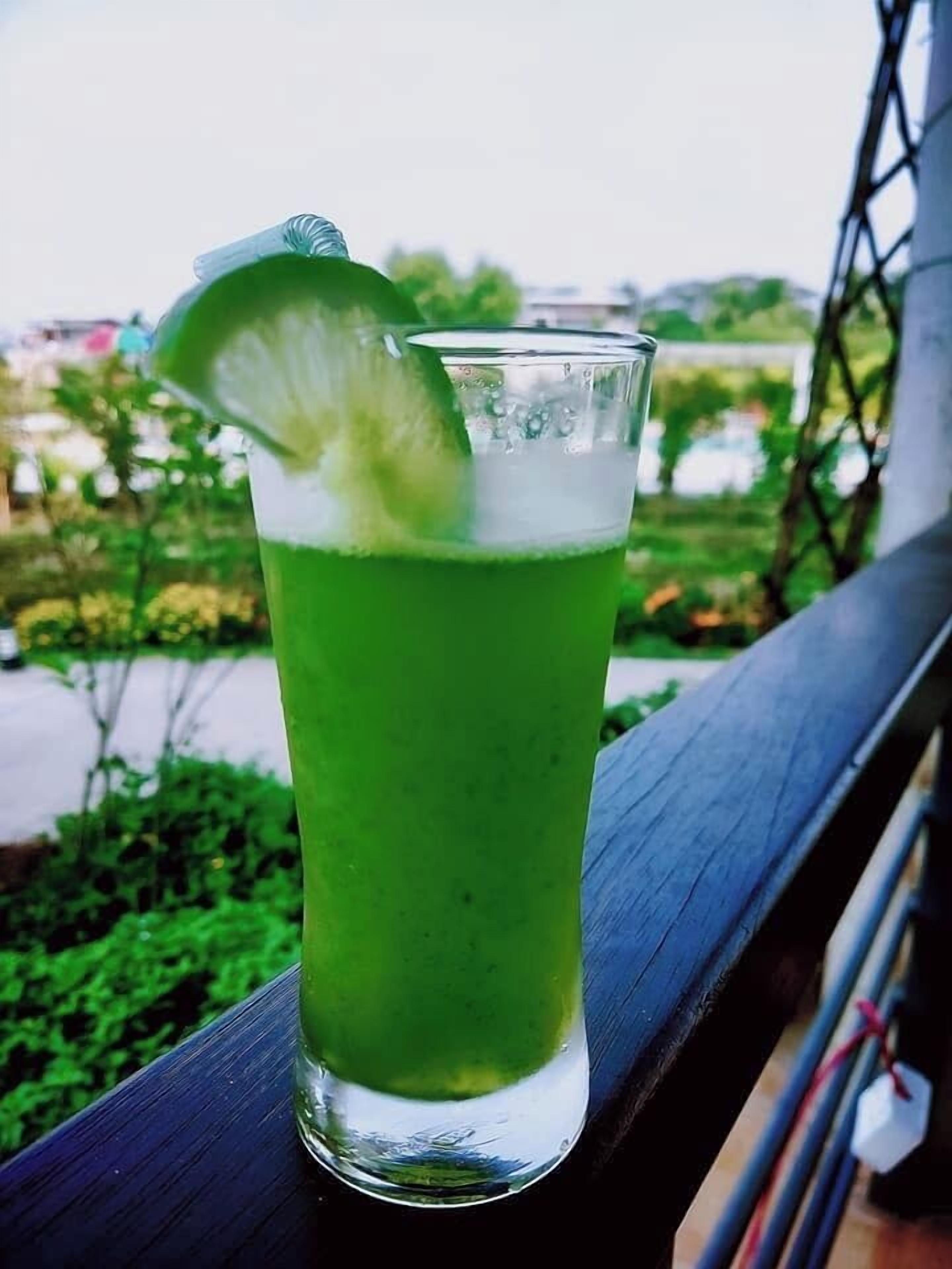 A tall glass with a green beverage, possibly a cocktail, garnished with a lime slice, placed on a wooden surface.
