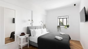 A modern bedroom with a bed, bedside table, and a window with plants. - Spacious & Modern 3BD Apt by Sea N' Rent (Tel Aviv)