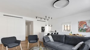 A modern living room with a grey sofa, two armchairs, a glass coffee table, and a dining area in the background. - Spacious & Modern 3BD Apt by Sea N' Rent (Tel Aviv)