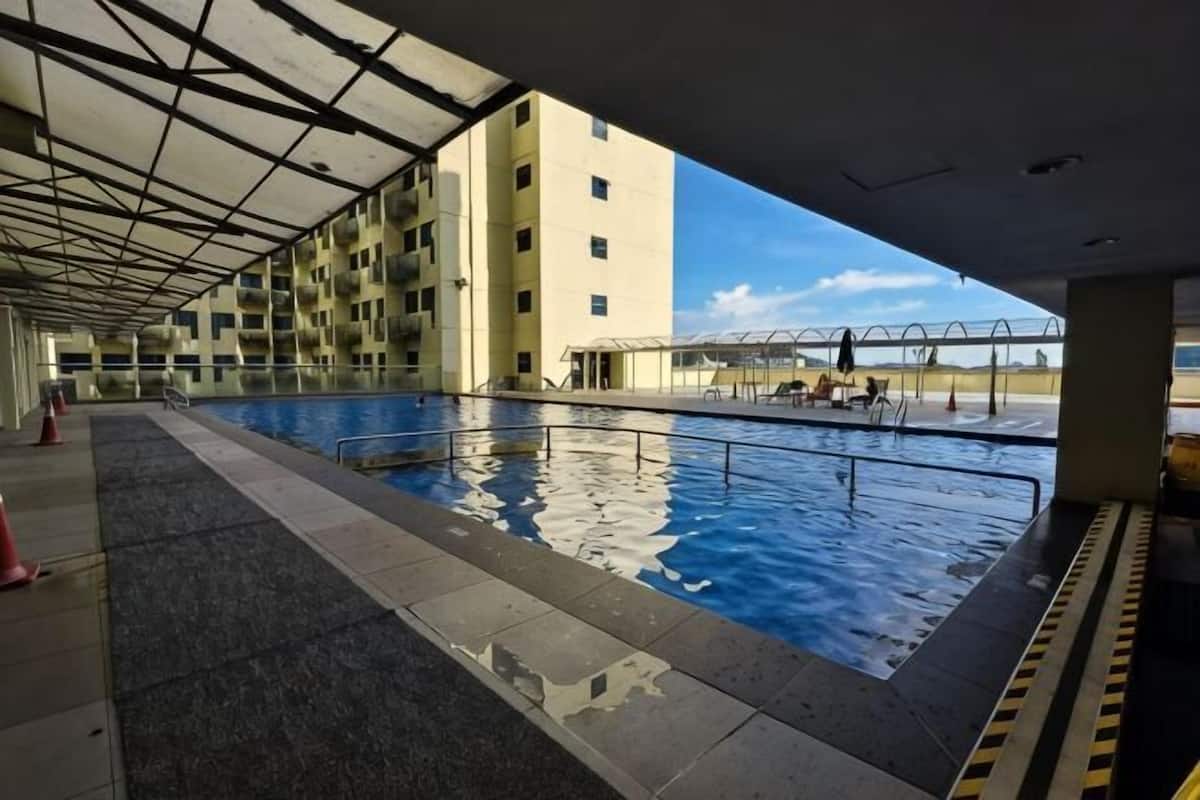 An indoor swimming pool with a view of a building, a covered walkway, and a clear sky.