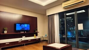 A modern living room with a flat-screen TV, a wooden entertainment unit, a glass door with a city view, and a small table. - South China Sea Place Suites by Kinabina Homestay (Kota Kinabalu)