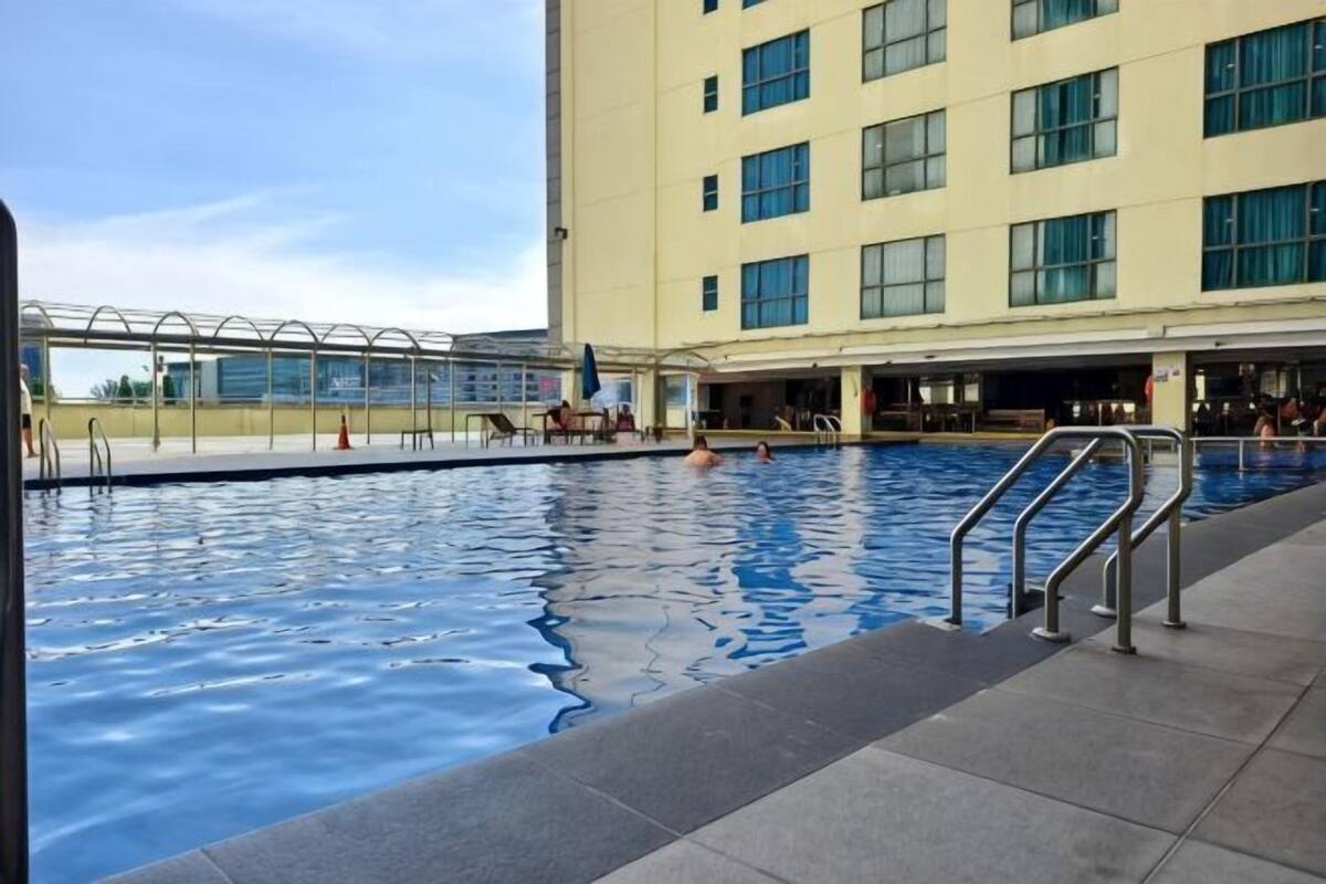 A swimming pool with a glass enclosure, a building with multiple windows, and a tiled deck area.