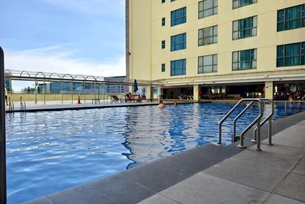 Ein Schwimmbecken mit Glasabdeckung, ein Gebäude mit vielen Fenstern und eine geflieste Terrassenfläche.