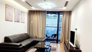 Ein modernes Wohnzimmer mit einer Ledersofa, einem Couchtisch, einem Flachbildfernseher und Blick auf eine Stadtlandschaft durch große Fenster.