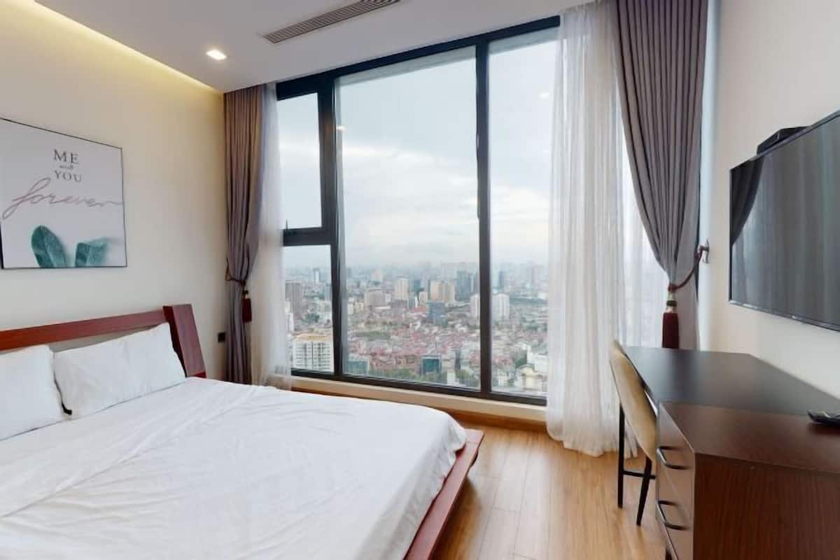 Een hotelkamer met een groot bed, een bureau, een televisie en uitzicht op de stad door grote ramen.