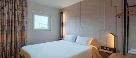A hotel room with a large bed, a desk, and a chair. There is a window with a view of a bridge, and the walls have a herringbone pattern.