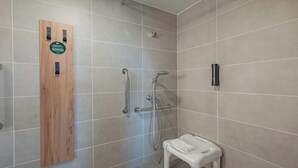 A shower area with a wooden panel, a handheld showerhead, a handheld showerhead, and a white stool. - B&B Hotel Macon Sud 3 étoiles (Vinzelles)