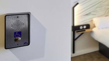 Una habitación de hotel con cama, mesita de noche y un intercomunicador en la pared.