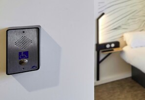 Una habitación de hotel con cama, mesita de noche y un intercomunicador en la pared.