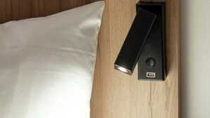 A bed with a white pillow and a black bedside table with a USB port. - B&B Hotel Macon Sud 3 étoiles (Vinzelles)
