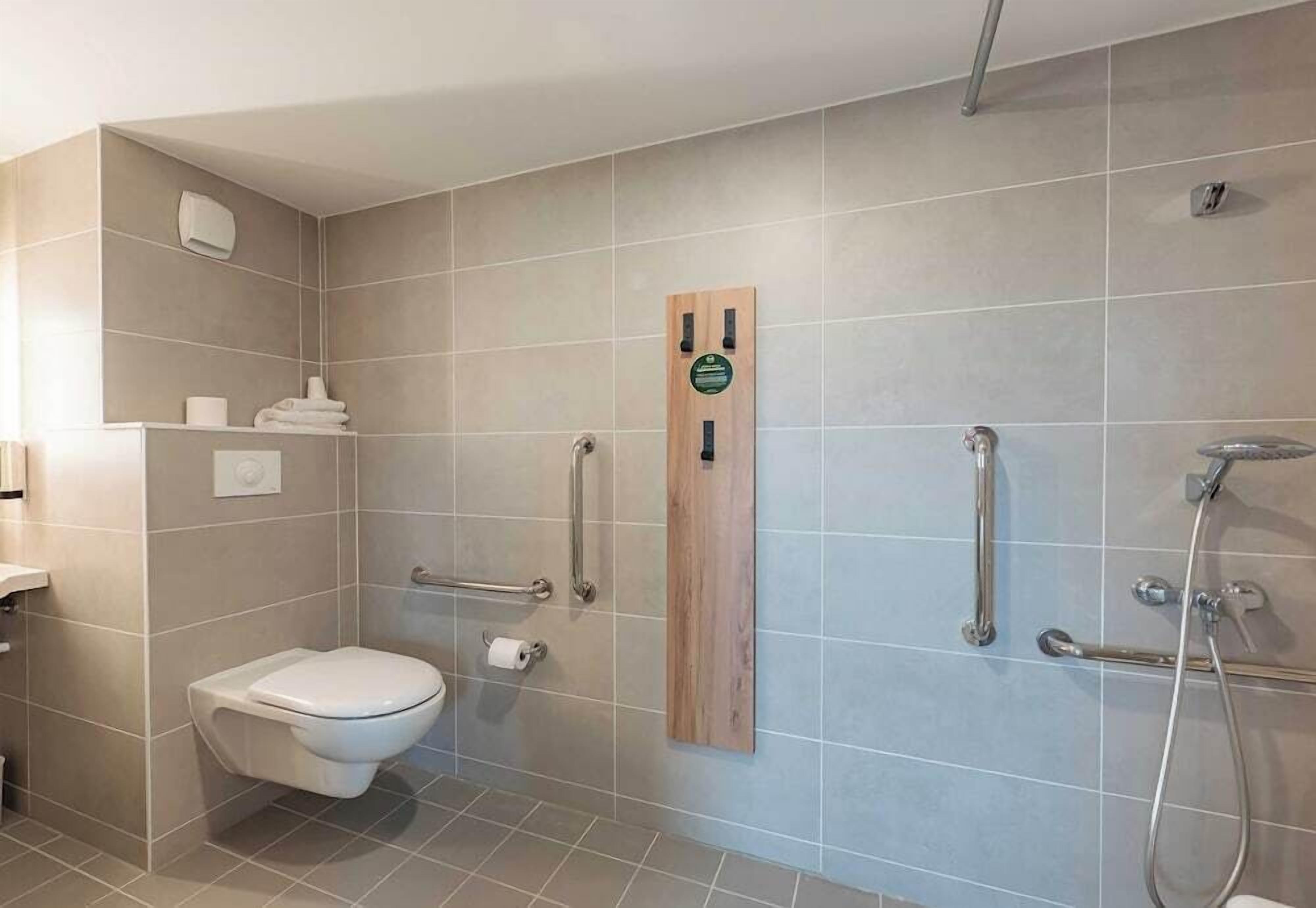 Un baño moderno con inodoro, ducha con barras de apoyo y un perchero para toallas.