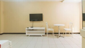 A room with a TV mounted on the wall, a white entertainment unit, two white chairs, and a small round table. - RedDoorz @ MUBG Apartelle near Baclaran Church (Paranaque)