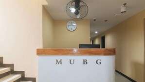 A reception desk with the letters "MUBG" on it, a clock on the wall, and a staircase leading up. - RedDoorz @ MUBG Apartelle near Baclaran Church (Paranaque)