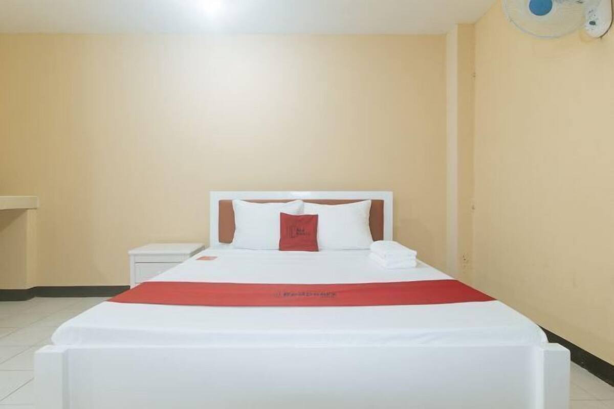 Habitació d'hotel amb llit, una taula de nit i un aparell d'aire condicionat fixat a la paret.