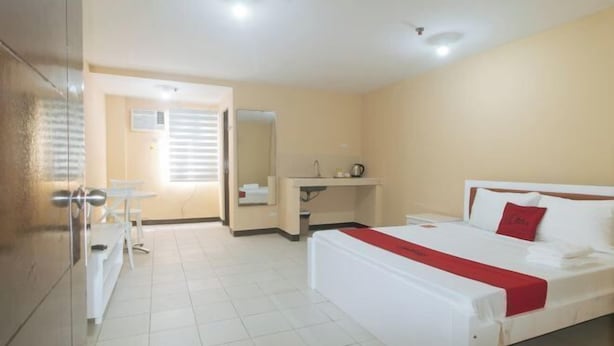 A hotel room with a bed, a desk, a chair, a mirror, and a window. - RedDoorz @ MUBG Apartelle near Baclaran Church (Paranaque)