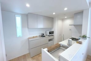 A compact kitchen with white cabinetry, a microwave, and a small countertop area. - New Garfieldhome Shinjuku (Tokyo)