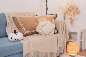 A blue sofa with a beige throw blanket, two decorative pillows, a small white pumpkin decoration, and a yellow woven lamp. - New Garfieldhome Shinjuku (Tokyo)