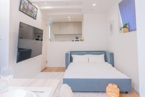 A bedroom with a bed, a flat-screen TV, a small kitchen area, and a window. - New Garfieldhome Shinjuku (Tokyo)